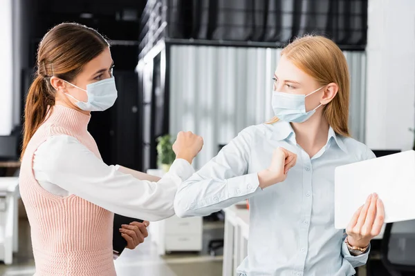 Бізнес-леді в медичних масках тримають цифровий планшет, даючи високі п'ять в офісі — стокове фото