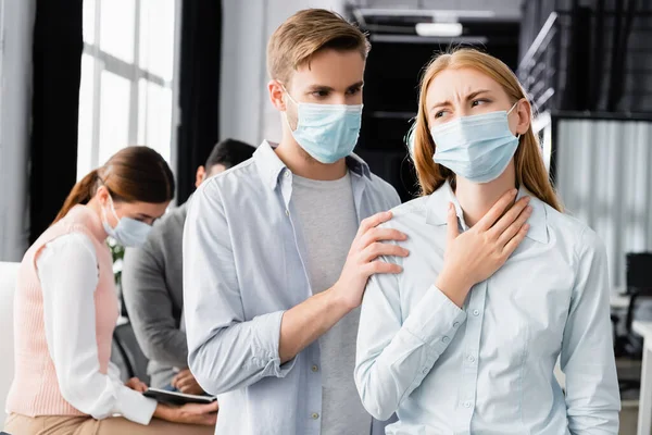 Empresario en máscara médica de pie cerca de colega enfermo en la oficina - foto de stock