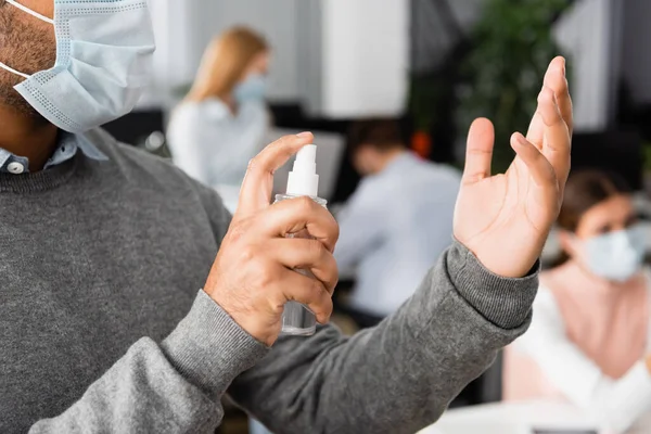 Vista ritagliata di uomo d'affari indiano in maschera medica utilizzando disinfettante per le mani in ufficio — Foto stock