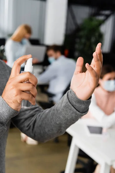 Vista recortada del empresario indio usando desinfectante de manos cerca de colegas en un fondo borroso en la oficina - foto de stock