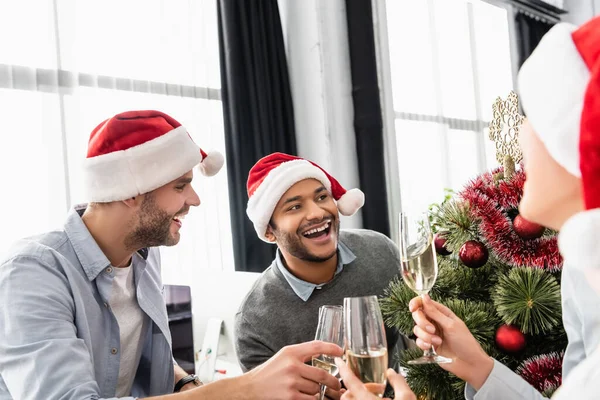 Negocios multiétnicos brindando con champán cerca del árbol de Navidad en la oficina - foto de stock