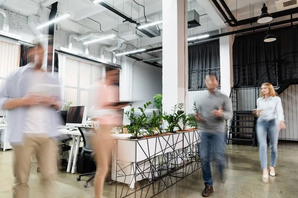 Desfoque de movimento de empresários caminhando perto de computadores e plantas no escritório — Fotografia de Stock