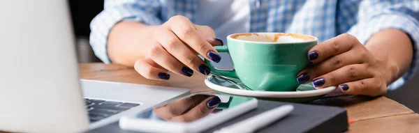 Partial view of freelancer near cup of coffee, laptop and smartphone on blurred foreground, banner — Stock Photo