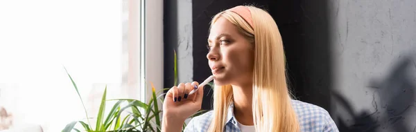 Joven rubia sosteniendo pluma y mirando hacia otro lado en la cafetería - foto de stock