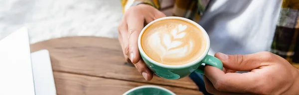 Обрізаний вид людини, що тримає чашку кави з латте мистецтвом, банер — стокове фото