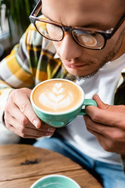 Close up view of man in eyeglasses holding cup of coffee with latte art — Stock Photo