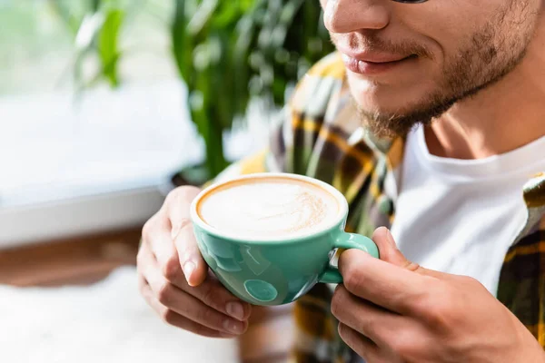 Abgeschnittene Ansicht eines verschwommenen jungen Mannes, der eine Tasse Kaffee mit Schaum hält — Stockfoto