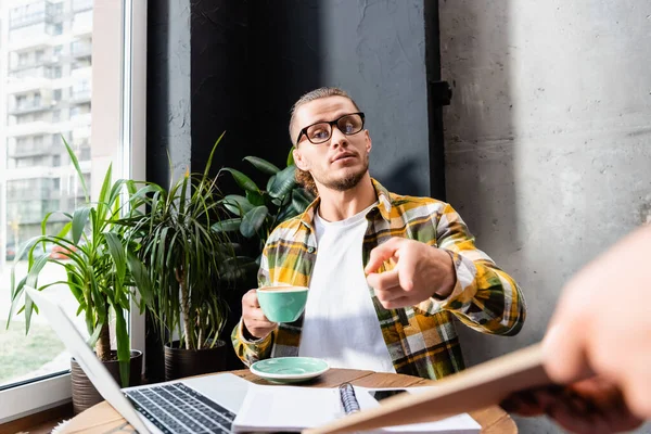 Junger Mann mit Brille zeigt mit Finger nahe Kellner auf verschwommenen Vordergrund — Stockfoto