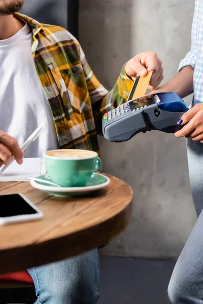 Vista cortada de garçom segurando terminal de pagamento perto do homem com cartão de crédito — Fotografia de Stock