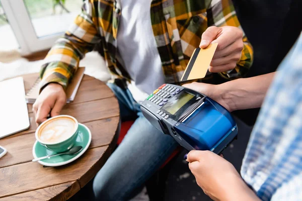 Vista cortada de barista segurando terminal de pagamento perto do cliente com cartão de crédito — Fotografia de Stock