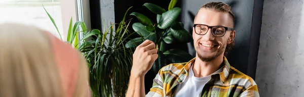 Cheerful young man in plaid shirt and eyeglasses smiling in cafe, banner — Stock Photo