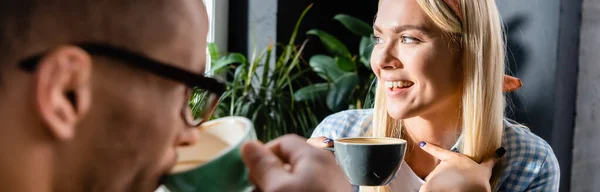 Donna allegra che tiene la tazza vicino all'amico che beve caffè in primo piano sfocato, banner — Foto stock