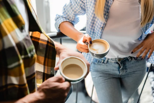 Cropped view of man and woman holding cups with cappuccino in cafe — Stock Photo