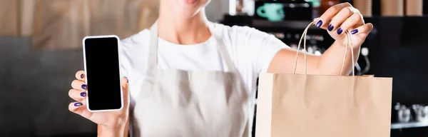 Cropped view of waiter holding paper bag and smartphone with blank screen, banner — Stock Photo