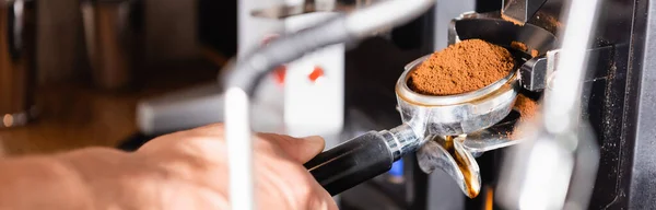 Partial view of barista holding portafilter with roasted ground coffee on blurred foreground, banner — Stock Photo