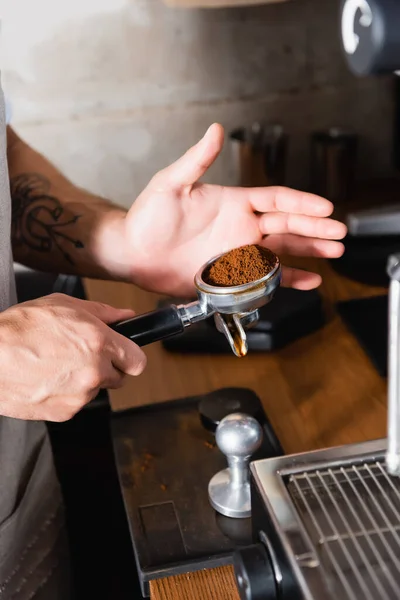 Vista cortada de tatuado barista segurando portafilter com café moído torrado — Fotografia de Stock