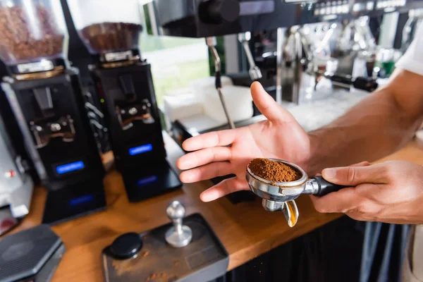 Partial view of barista holding portafilter with roasted ground coffee near coffeemaker — Stock Photo