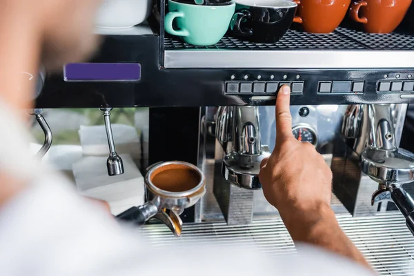 Vue recadrée du bouton-poussoir barista sur la machine à café tout en tenant le filtre portatif, avant-plan flou — Photo de stock