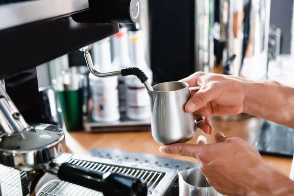 Vue recadrée du barista tenant une tasse de lait métallique près du vapeur de la machine à café — Photo de stock