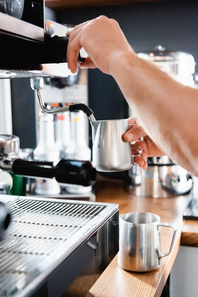 Vista parziale di barista che tiene tazza di latte metallico vicino al vapore della caffettiera — Foto stock