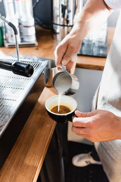 Vista cortada de barista derramando leite de caneca metálica em xícara com café — Fotografia de Stock