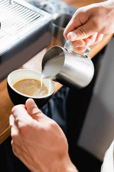 Vista cortada de barista derramando leite de caneca metálica em xícara com café — Fotografia de Stock