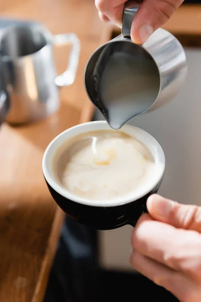 Visão parcial de barista derramando leite em xícara com café — Fotografia de Stock