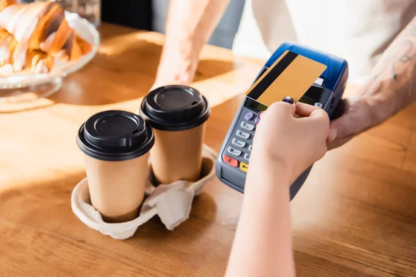 Partial view of woman holding credit card near barista with payment terminal on blurred background — Stock Photo