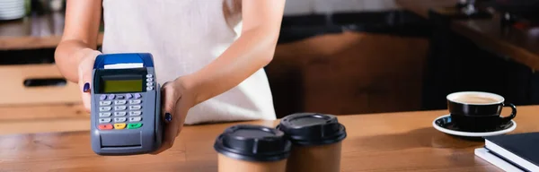 Partial view of barista holding payment terminal near coffee to go on blurred foreground, banner — Stock Photo