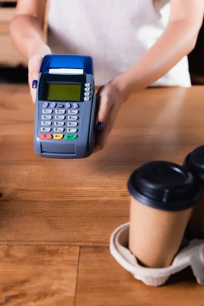 Cropped view of waiter holding payment terminal near coffee to go on blurred foreground — Stock Photo