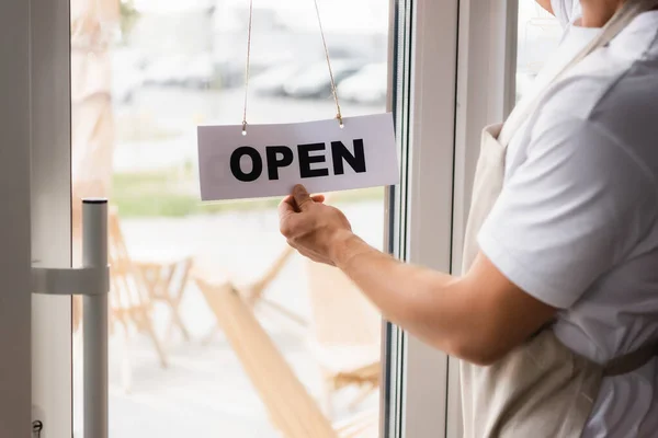 Cropped view of barista touching card with open lettering hanging on cafe entrance door — Stock Photo