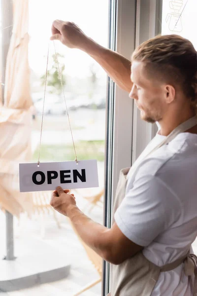 Young barista holding card with open lettering near cafe entrance door — Stock Photo