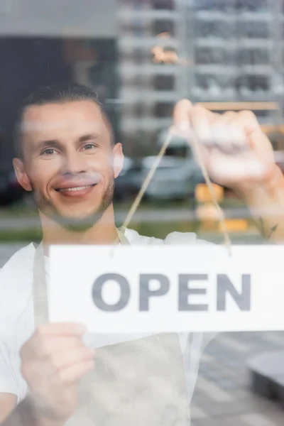 Happy barista hanging card with open lettering on cafe entrance door — Stock Photo