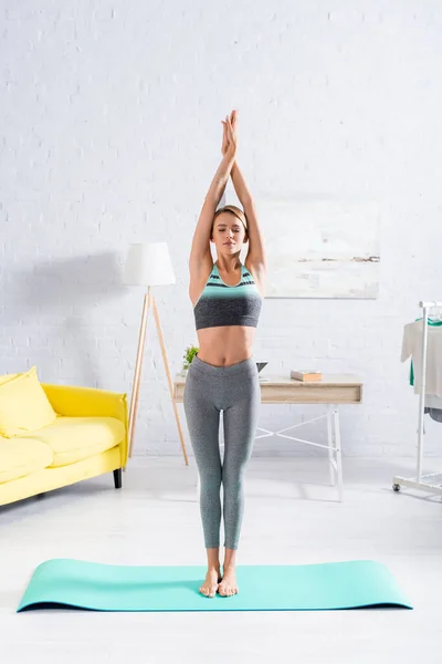 Femme blonde avec les yeux fermés pratiquant le yoga sur tapis de fitness à la maison — Photo de stock