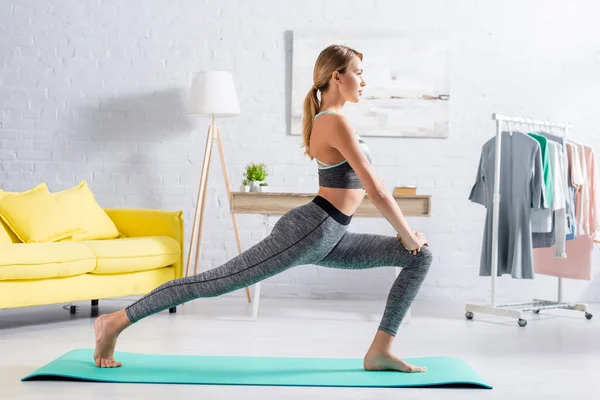 Vista laterale della sportiva a piedi nudi che pratica yoga a casa — Foto stock