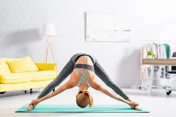 Mujer joven flexing mientras practica yoga en la sala de estar - foto de stock