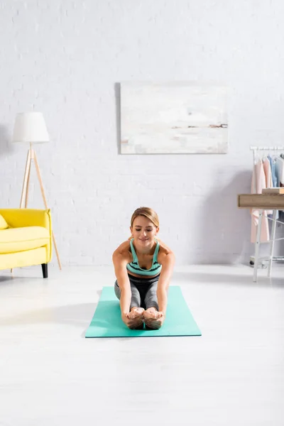 Esportista sorrindo alongamento durante o exercício de ioga no tapete de fitness — Fotografia de Stock