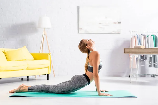 Mujer en ropa deportiva haciendo yoga asana con los ojos cerrados en la esterilla de fitness - foto de stock