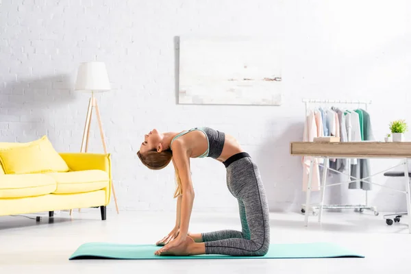 Side view of blonde sportswoman bending back during yoga exercise at home — Stock Photo