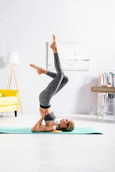 Vista lateral de una joven deportista con las piernas levantadas haciendo ejercicio de yoga - foto de stock