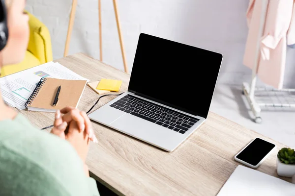 Laptop, smartphone and papers on table near teleworker in headset on blurred foreground — Stock Photo