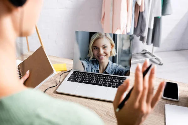 Freelancer holding notebook and pen while using headset and having video call on laptop — Stock Photo