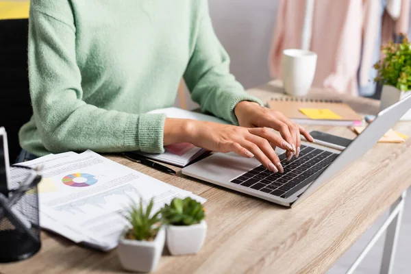 Ausgeschnittene Ansicht von Freelancer mit Laptop in der Nähe von Papieren mit Diagrammen im unscharfen Vordergrund — Stockfoto