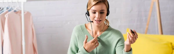 Smiling woman holding pen while using headset at home, banner — Stock Photo