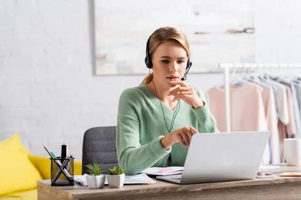 Blonde freelancer in headset having video chat on laptop on blurred foreground — Stock Photo