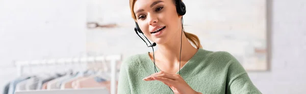 Smiling freelancer in headset using laptop on blurred foreground at home, banner — Stock Photo