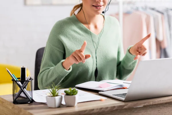 Cropped view of freelancer in headset pointing with fingers during video call on laptop on blurred foreground — Stock Photo