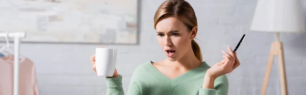 Mulher confusa segurando copo e caneta em casa, banner — Fotografia de Stock