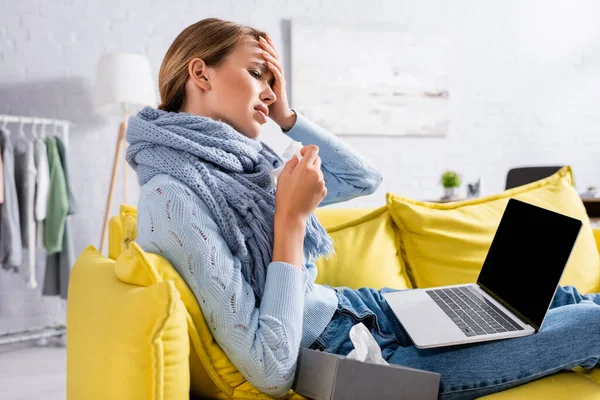 Sick woman holding napkin near laptop with blank screen on couch — Stock Photo