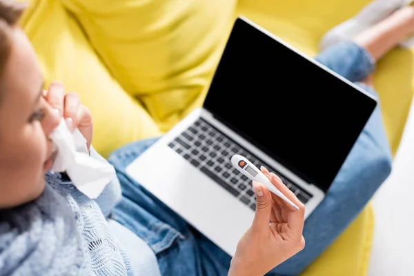 Termômetro na mão de freelancer doente segurando guardanapo com laptop borrado no fundo — Fotografia de Stock